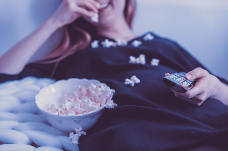 Woman eating popcorn while watching tv on the couch