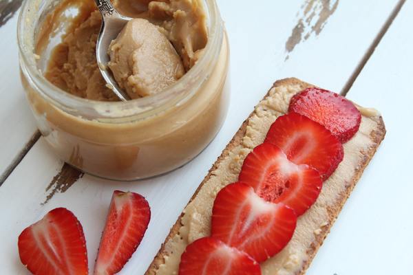 Nut butter in an unlabled jar next to cracker with nut butter and thin-sliced strawberries