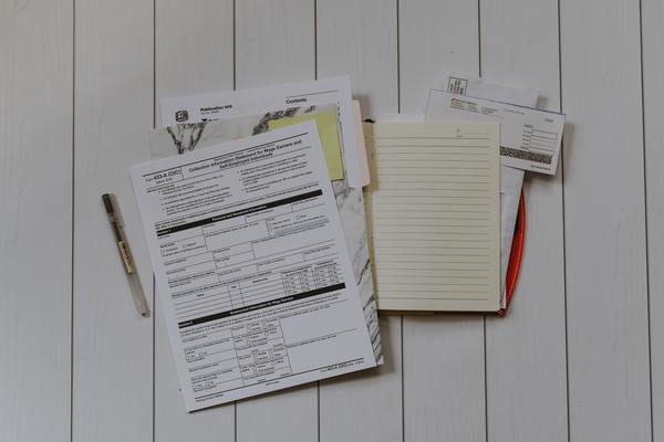 Blank forms, notebook paper, checks, and pens on a white table.